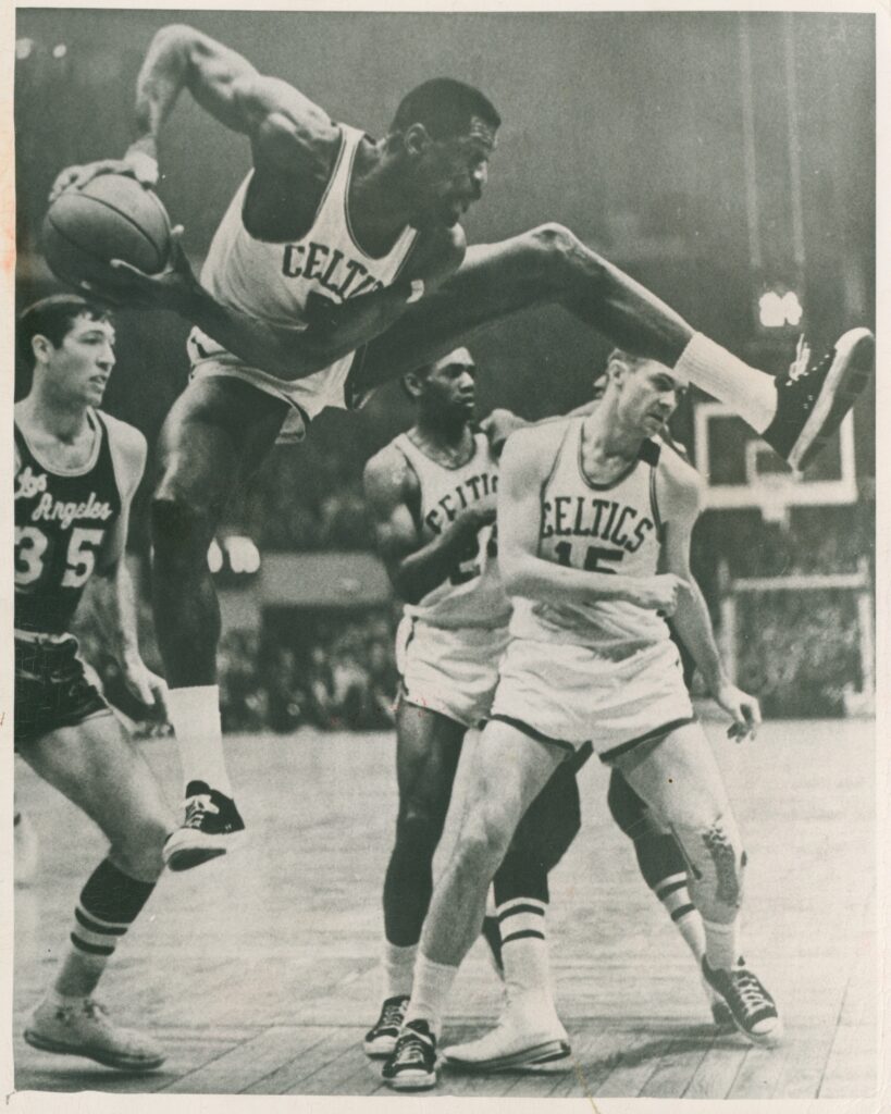 黑白图像的比尔-拉塞尔身穿白色凯尔特人均匀张开双腿的球而跳跃。