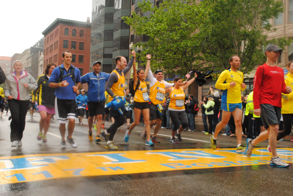 几个人跑在黄色和蓝色的波士顿马拉松比赛的终点线。